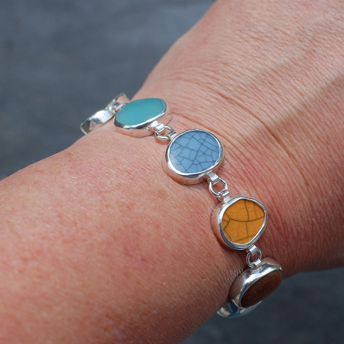 Silver bezel set bracelet with sea glass and pottery pieces being worn on a wrist.