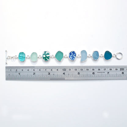 Blue and green sea glass and pottery shard bracelet on a white background with ruler.