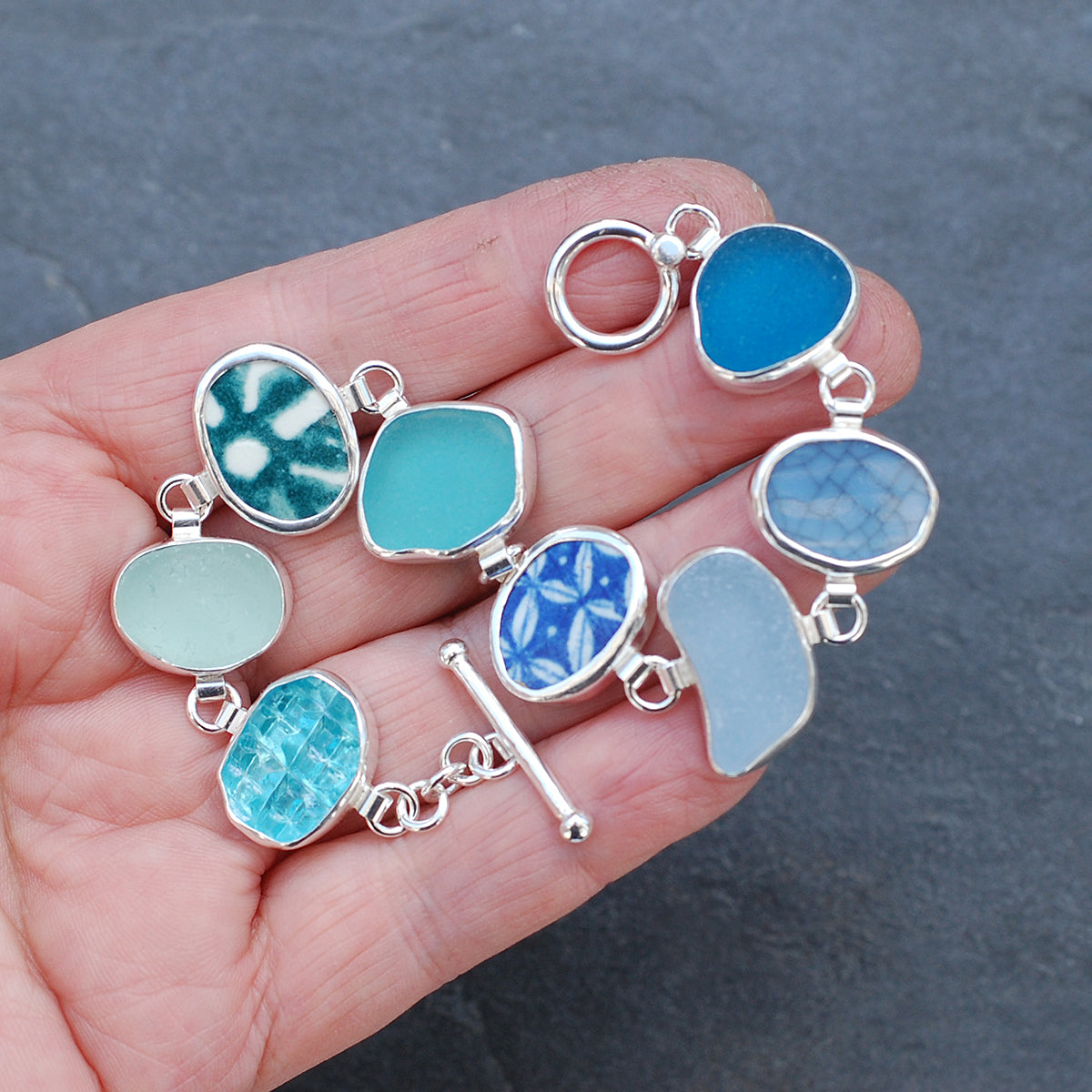 Blue and green sea glass and pottery shard bracelet on a hand