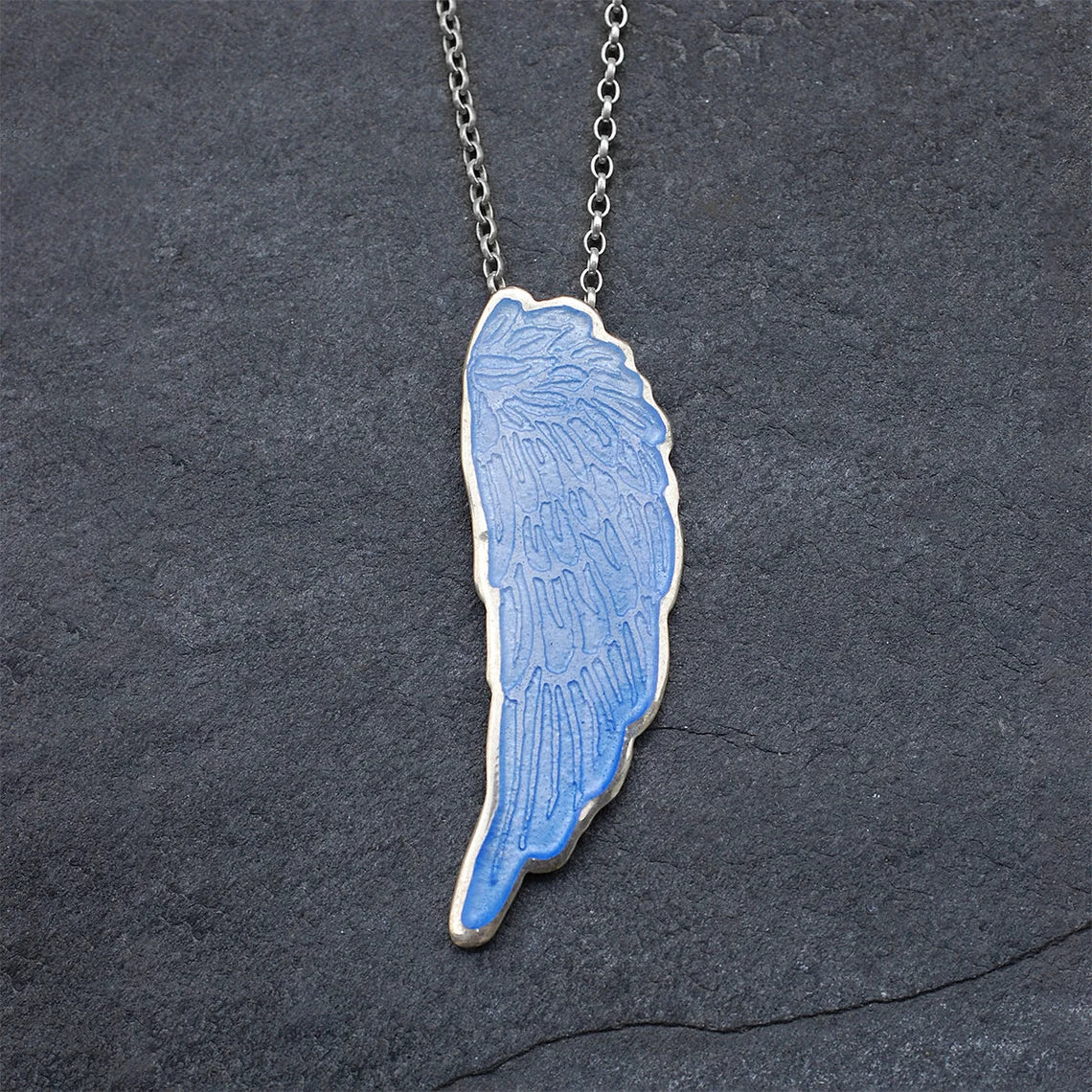 Blue Enamelled Angel Wing Pendant on a grey slate background