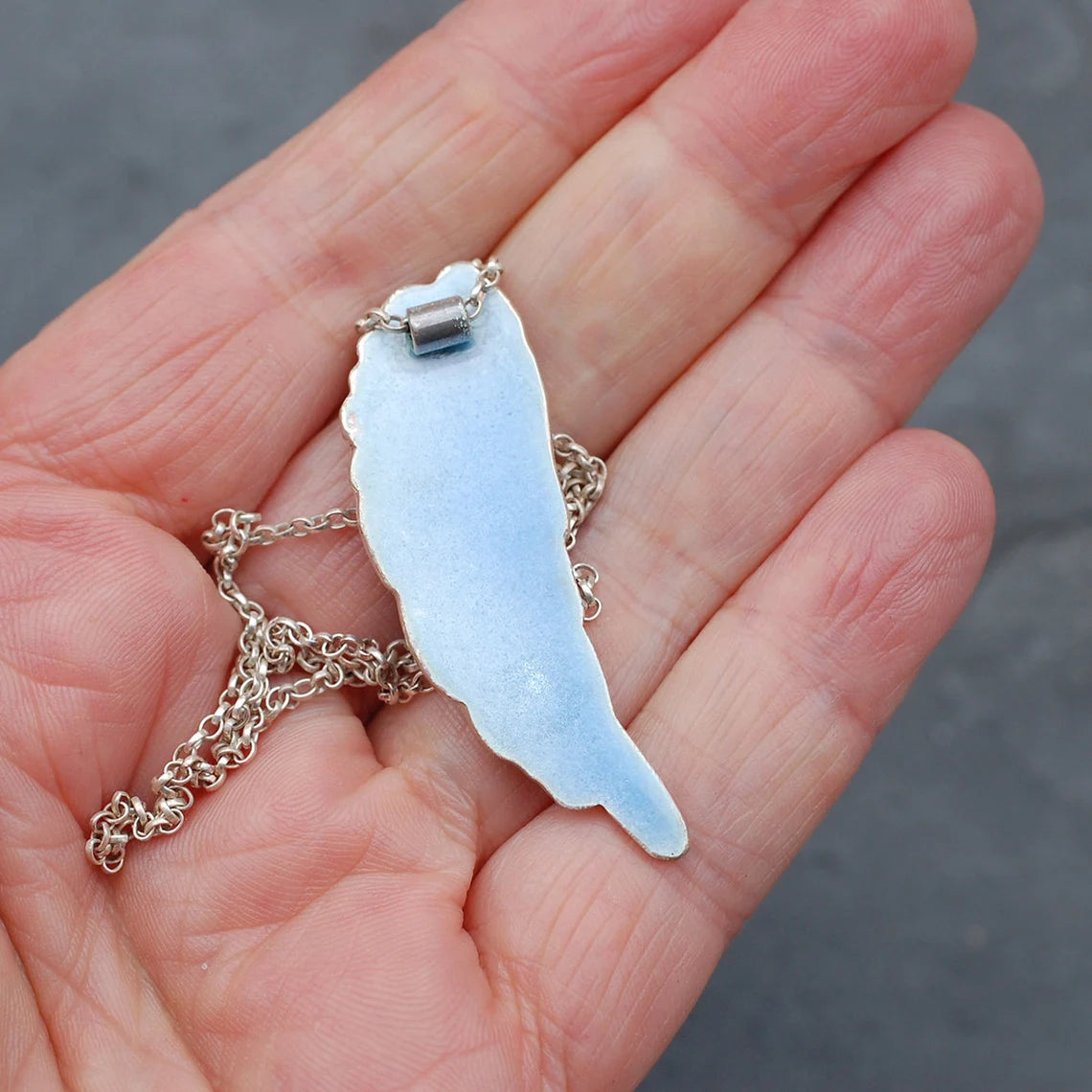 Blue Enamelled Angel Wing Pendant on a hand to show size - back view.