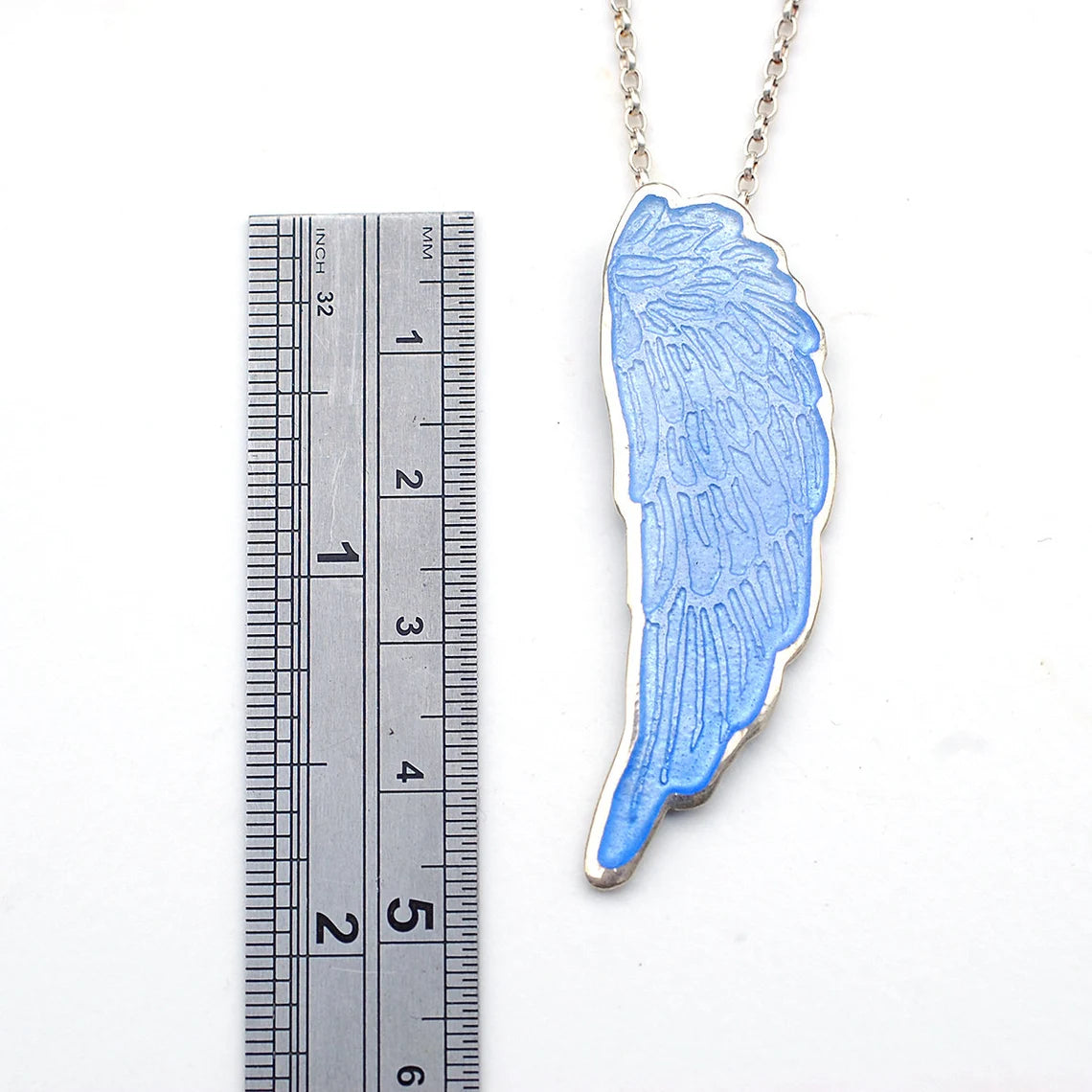 Blue Enamelled Angel Wing Pendant on a white background with ruler, to show the size.