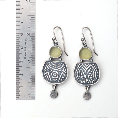 Etched silver earrings with olive green sea glass,  on a white background, with a ruler