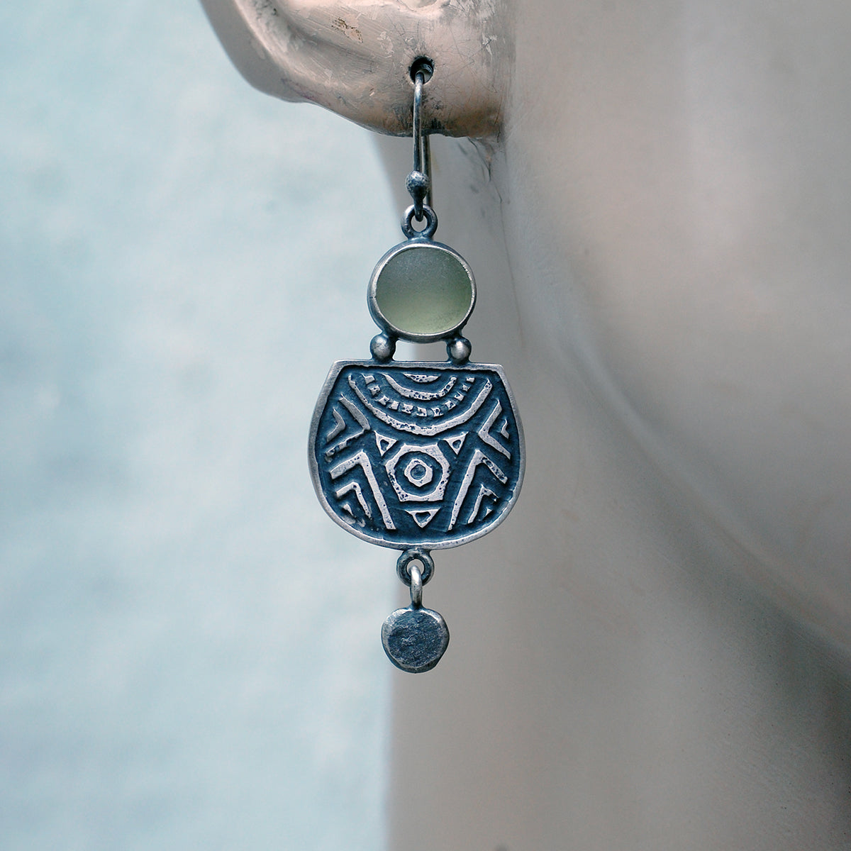 Etched silver earrings with olive green sea glass,  on a mannequin.