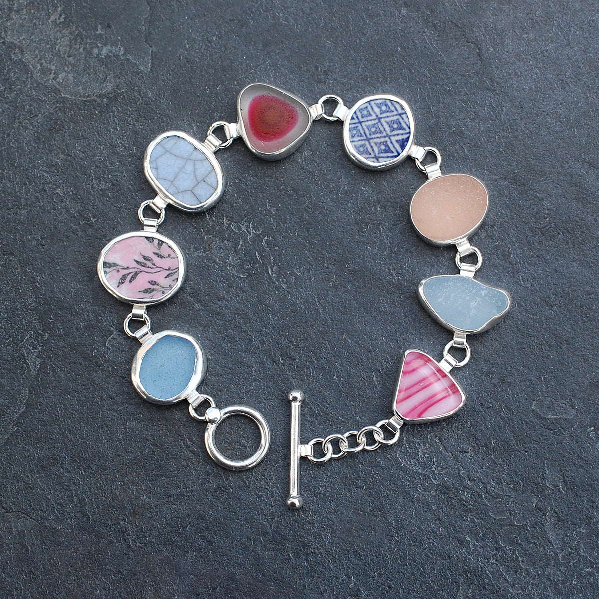 Pink and blue sea glass and pottery shard bracelet on a slate grey background.