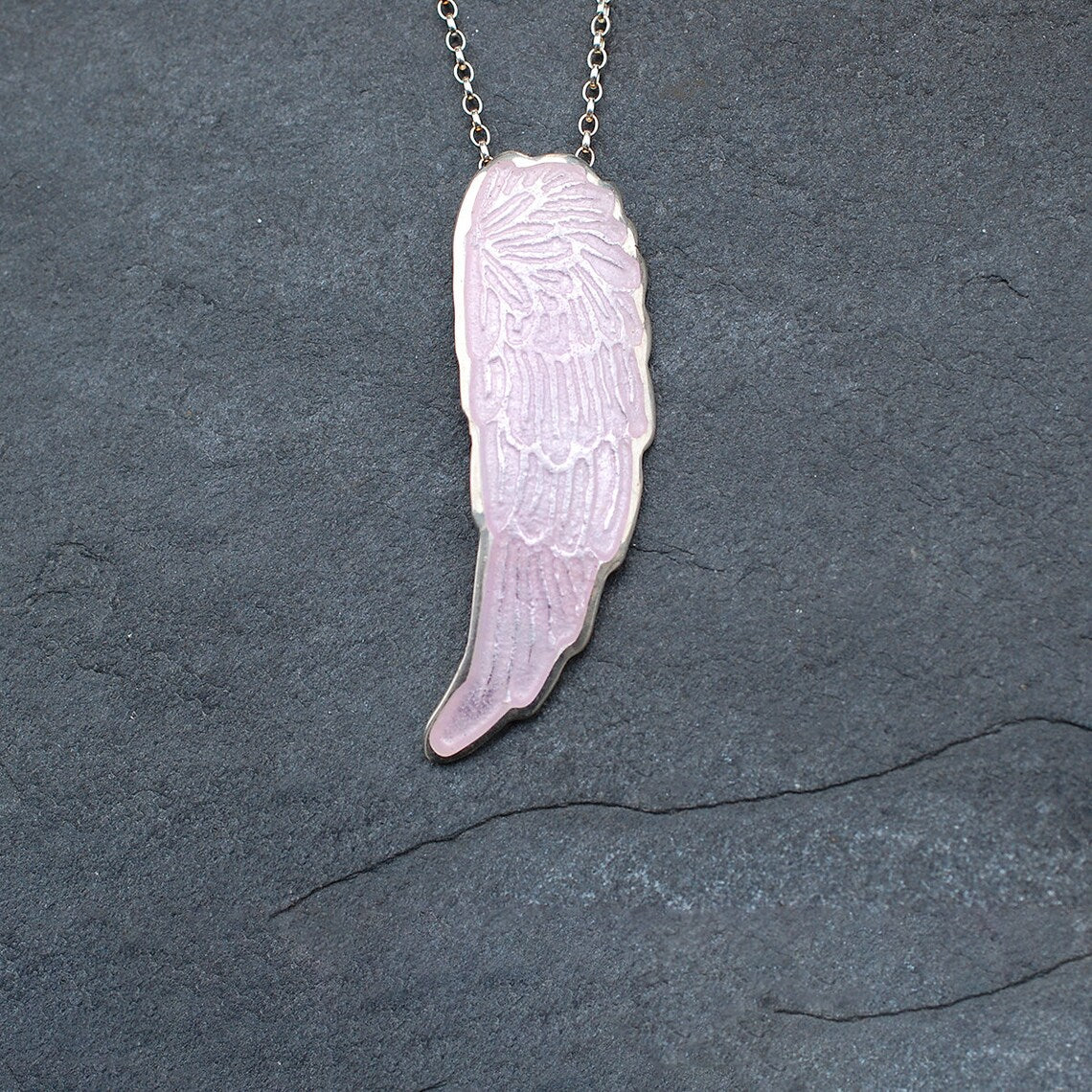 Silver and pink enamel angel wing pendant on a slate grey background.