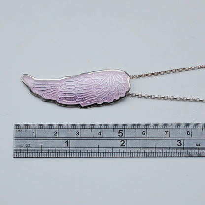 Silver and pink enamel angel wing pendant on a white background, with ruler