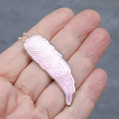 Silver and pink enamel angel wing pendant on a hand