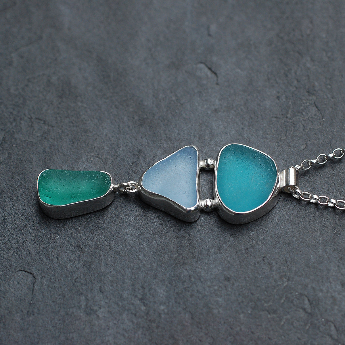 Triple sea glass pendant on a grey slate background, side view